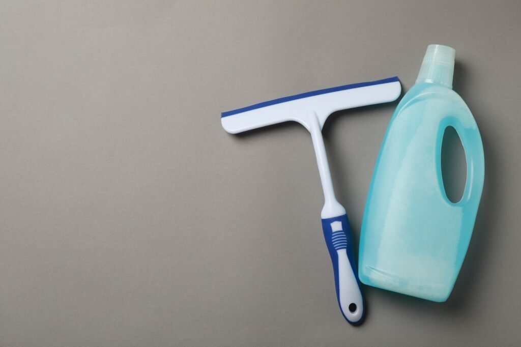 Detergent and window cleaning squeegee on gray background